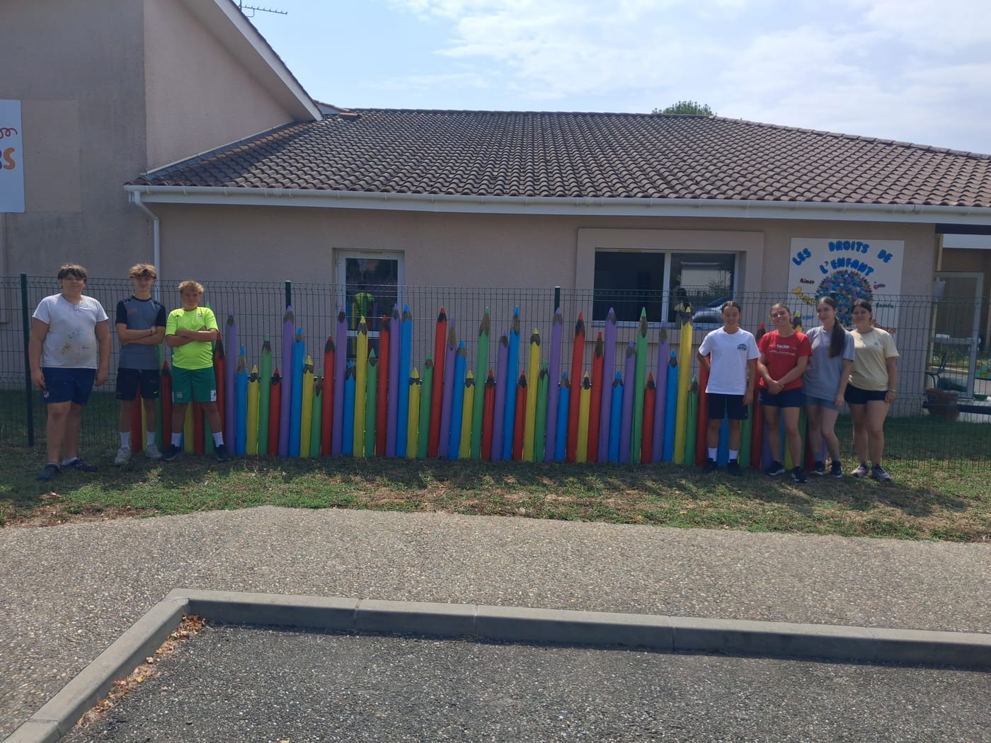 Sept adolescents du chantier citoyen posent devant la clôture de l'école, qu'ils ont habillée de crayons de couleur géants peints de toutes les couleurs.